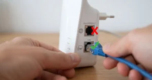 Close em mãos conectando um cabo de rede RJ45 na porta LAN de um repetidor Wi-Fi, indicando com um ícone verde a escolha correta e um vermelho na porta WAN.